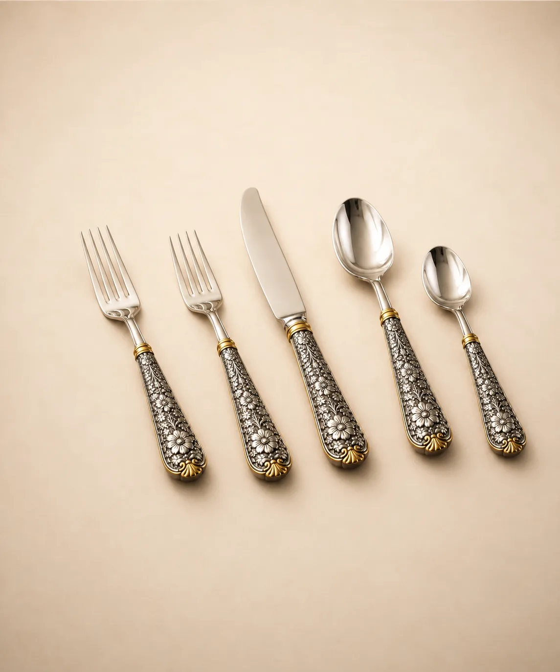 Sterling silver cutlery set with floral repoussé handles and gold detailing, handcrafted in Jaipur.